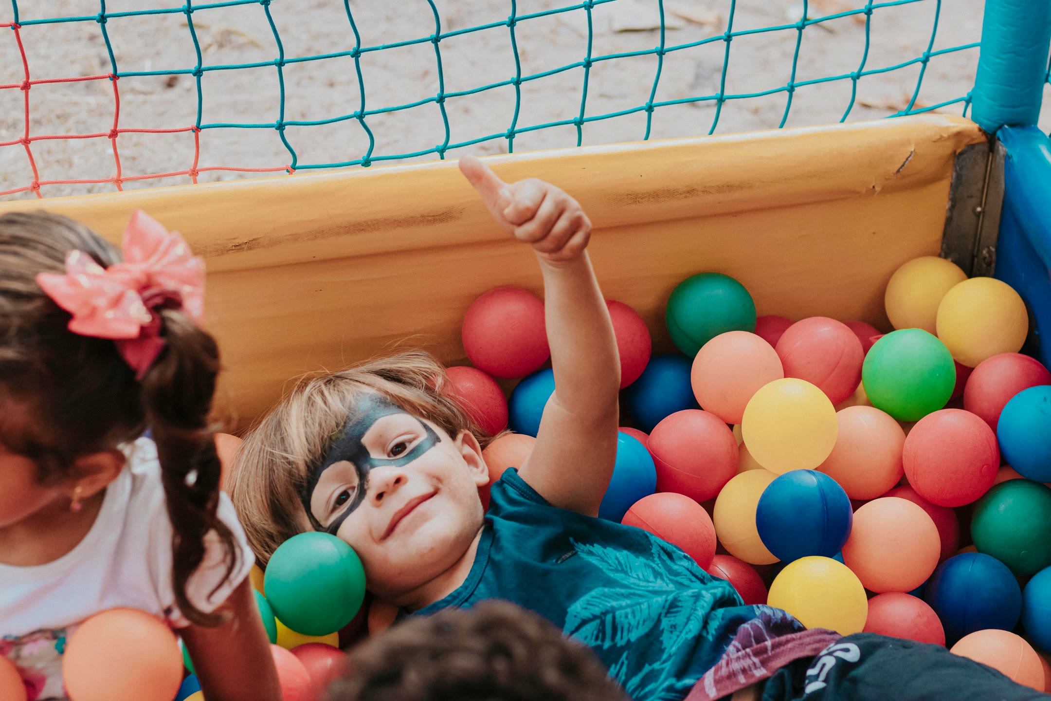 carlos-magno-DzcULYvMSYY-unsplash-optimized Child with their thumb up while in a ball pit at a playground